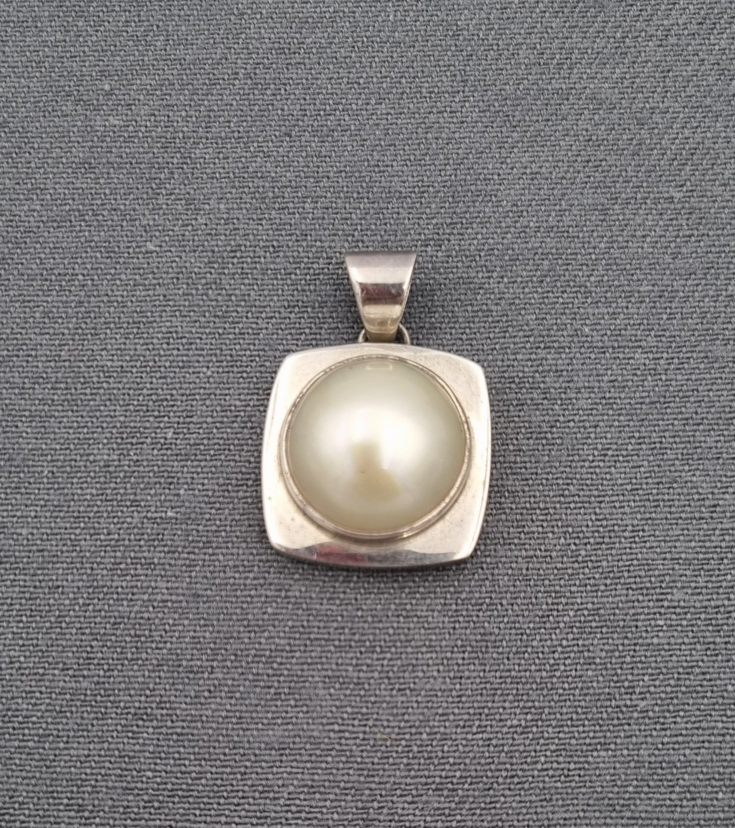 A mabe' pearl set in a sterling silver square setting with a bold design, displayed against a grey background.