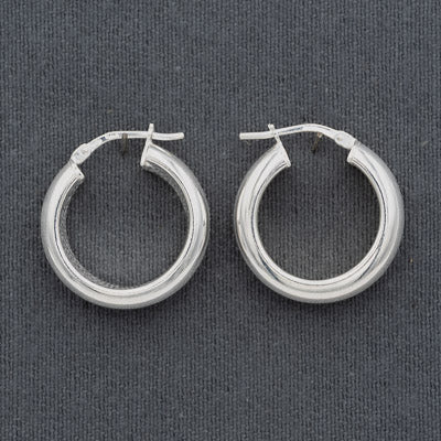 A pair of polished silver hoop earrings with a textured, ribbed outer band and a smooth inner band, displayed on a dark gray textured fabric background.