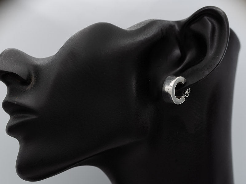 A silver hoop earring with a small infinity symbol on the inner band, shown on a black mannequin head in profile against a light gray background.