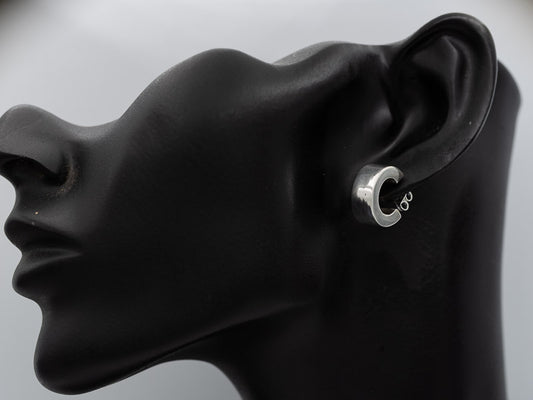 A silver hoop earring with a small infinity symbol on the inner band, shown on a black mannequin head in profile against a light gray background.