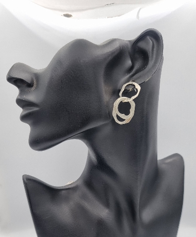 A pair of silver-toned abstract dangle earrings displayed on a black mannequin head against a white background.