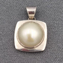 A mabe' pearl set in a sterling silver square setting with a bold design, displayed against a grey background.