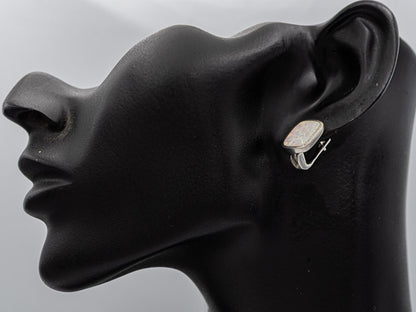 A silver-toned hoop earring with a rectangular, textured cream-colored stone, displayed on a black mannequin head in profile against a light gray background.