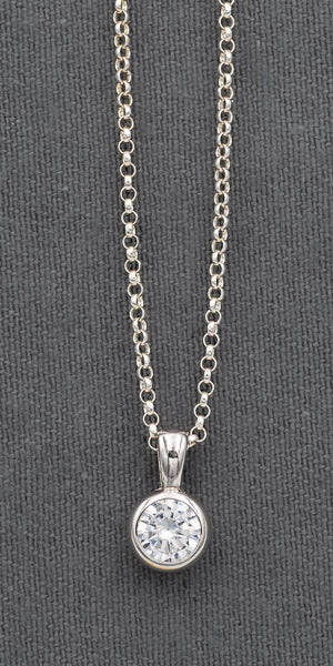 A silver necklace with a round bezel-set clear gemstone pendant, displayed against a dark gray textured background.