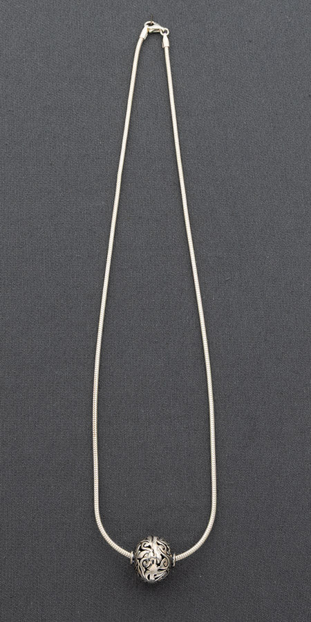 A silver-toned snake chain necklace with a single round, textured silver bead pendant, displayed against a dark gray background.