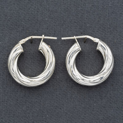 A pair of textured silver hoop earrings with a twisted, braided design, displayed on a dark gray fabric background.