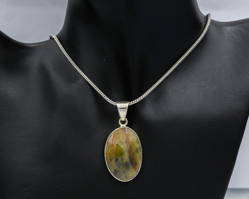 A silver chain necklace with an oval pendant featuring a marbled green, yellow, and brown stone, displayed on a black mannequin bust.